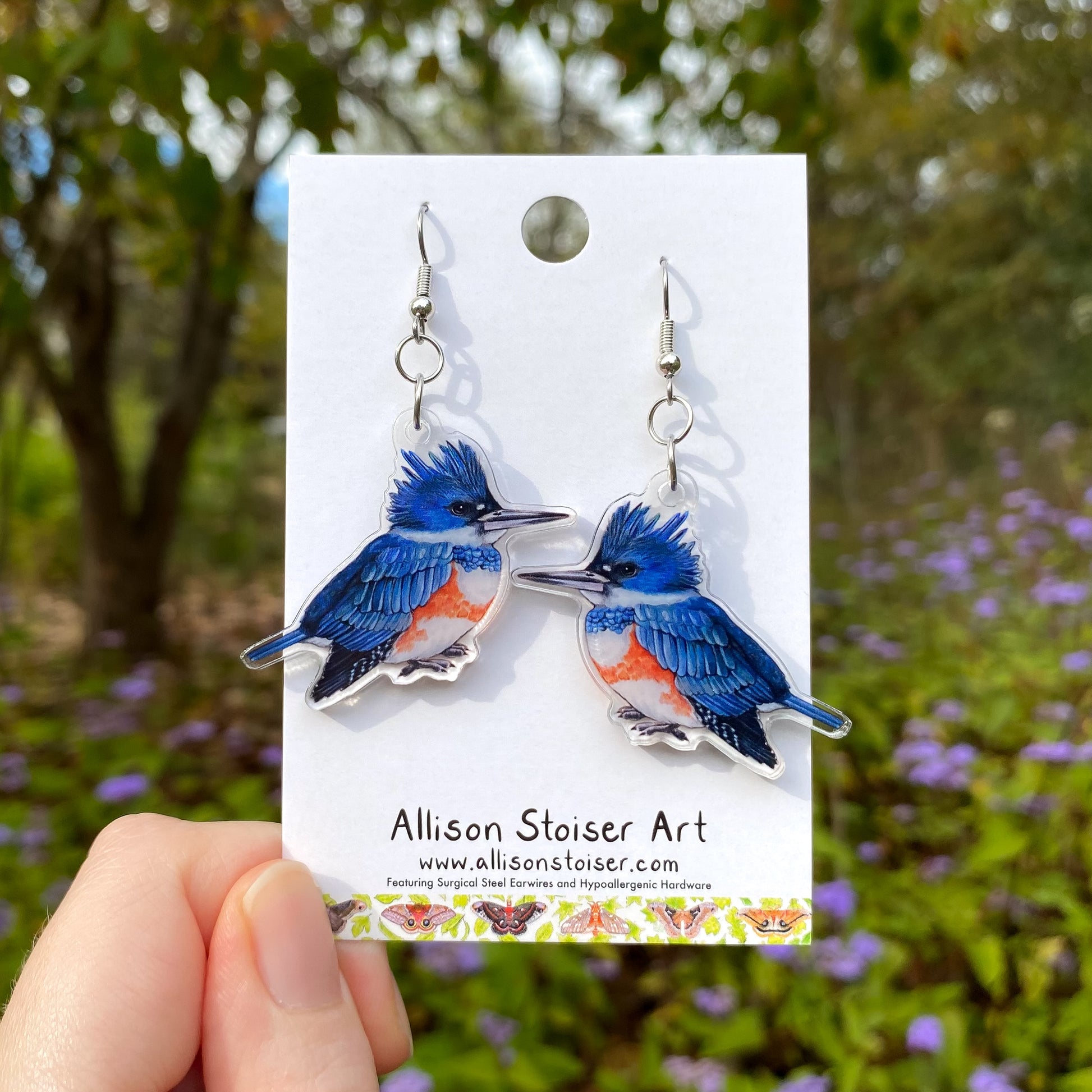 Female belted kingfisher earrings on a card held by a hand with a natural background