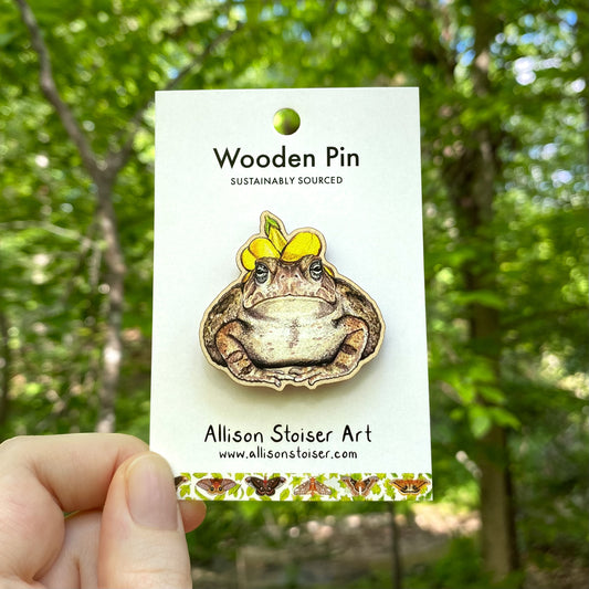 A wooden pin of a Fowler’s toad wearing a flower hat