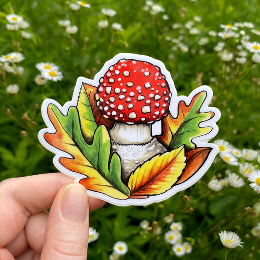 Sticker of a red fly agaric mushroom held in front of a green field with white flowers.