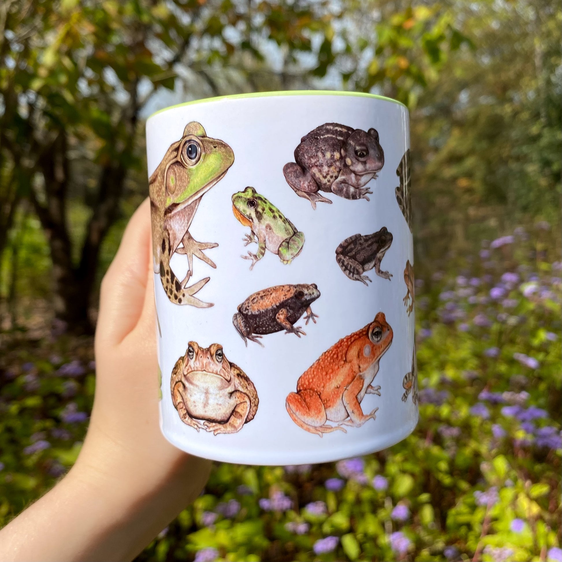 Mug with frog illustrations held in a hand against a natural background