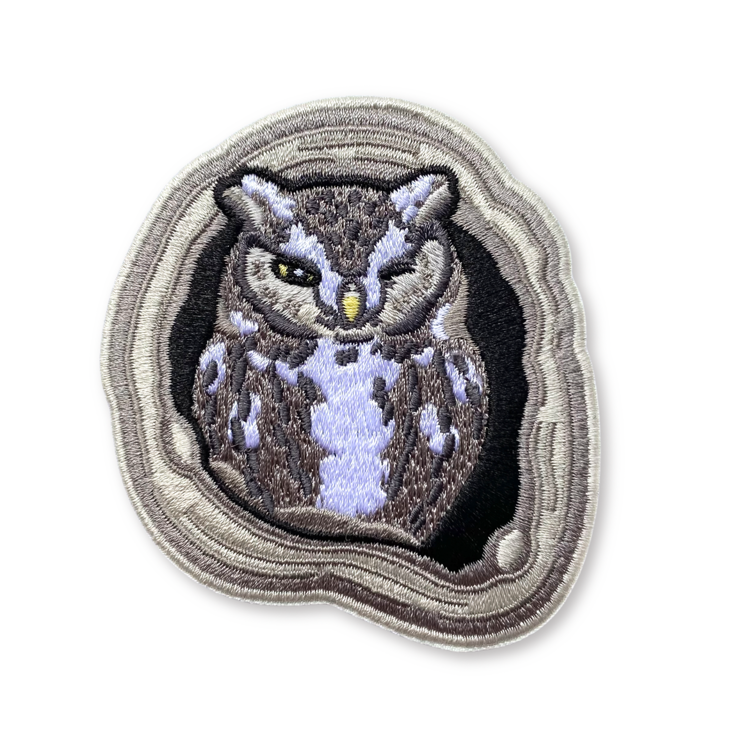 Embroidered patch of an owl in a tree hole on a white background