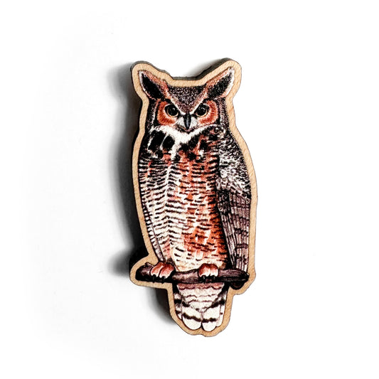 A hand holds a sustainably sourced wooden pin featuring an illustration of a great horned owl pin