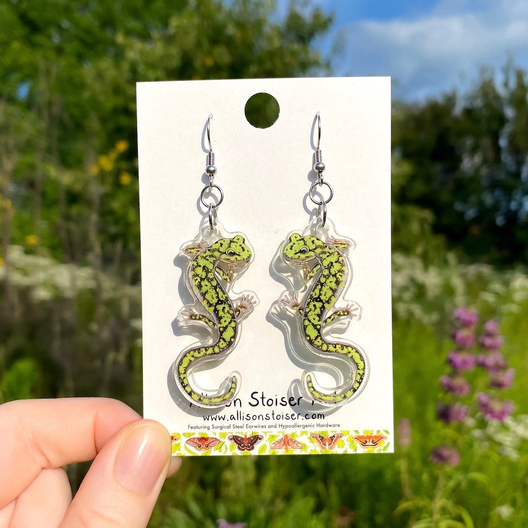 A hand holding a pair of acrylic green salamander earrings.