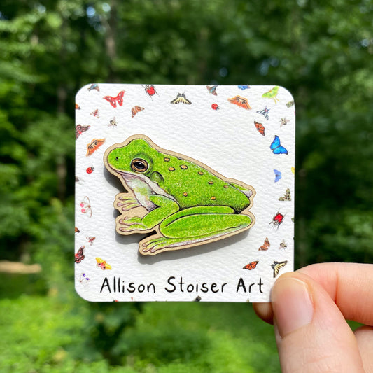 A wooden pin of an American green tree frog on a white background.