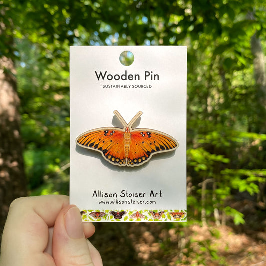 A wooden pin of an orange gulf fritillary butterfly on packaging that reads Wooden Pin, Sustainably Sourced.