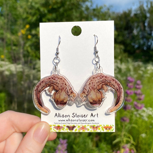 A hand holding a pair of acrylic hellbender earrings.