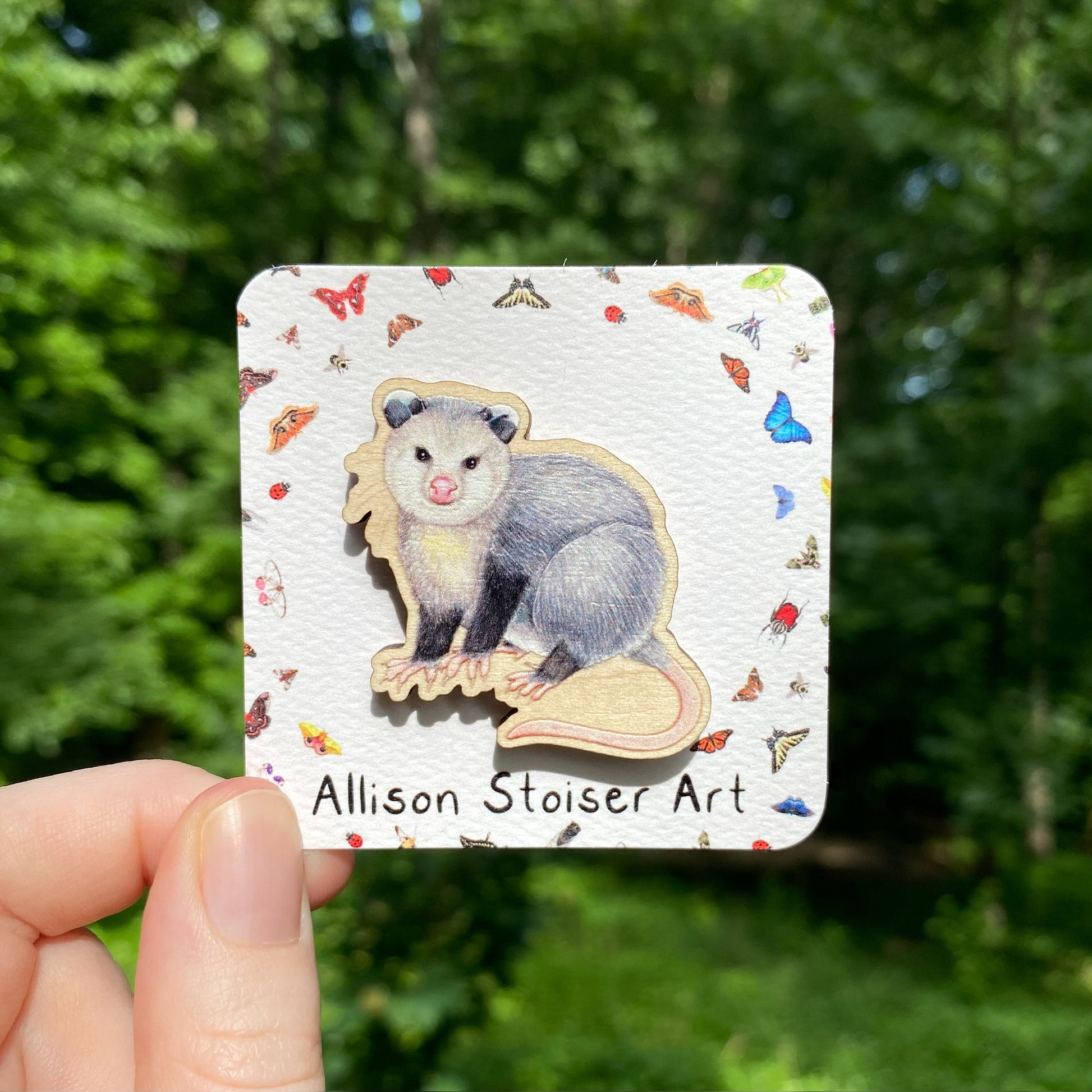 A hand holding a wooden pin of a Virginia opossum.