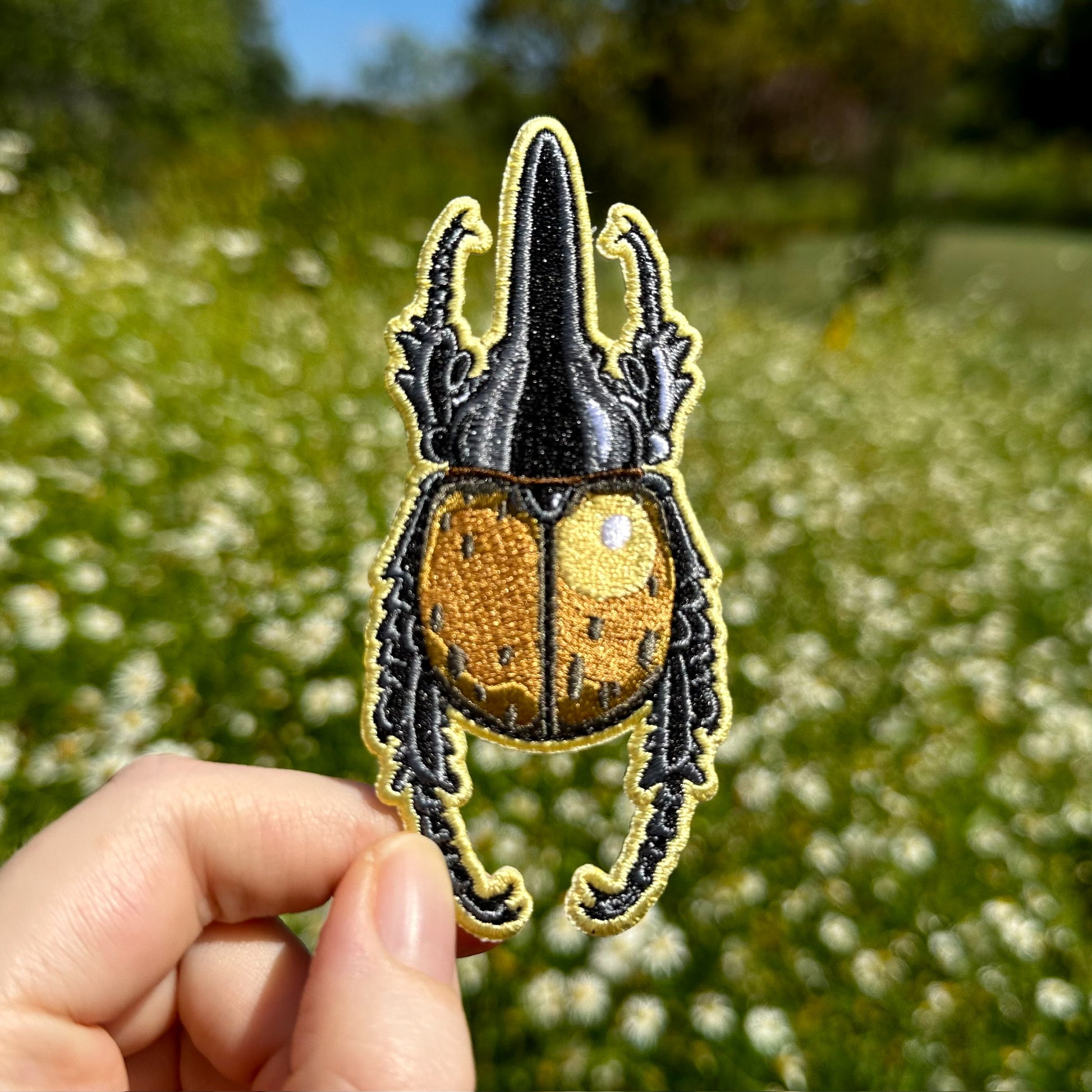 A hand holding an embroidered patch of a Hercules beetle