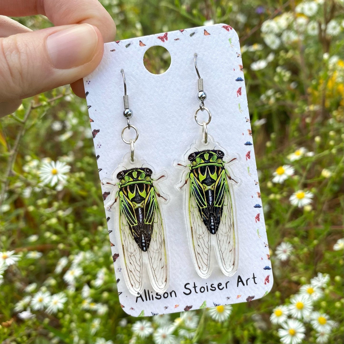 A hand holding a pair of linne's cicada acrylic earrings