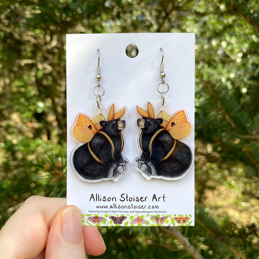 A hand holding a pair of acrylic io moth bear earrings