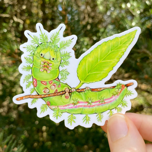 A hand holding a sticker of an io moth caterpillar