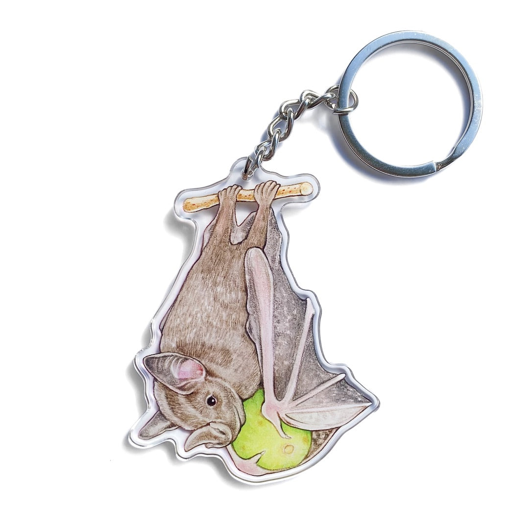 A keychain of a Jamaican fruit bat snacking on a fig on a white background.