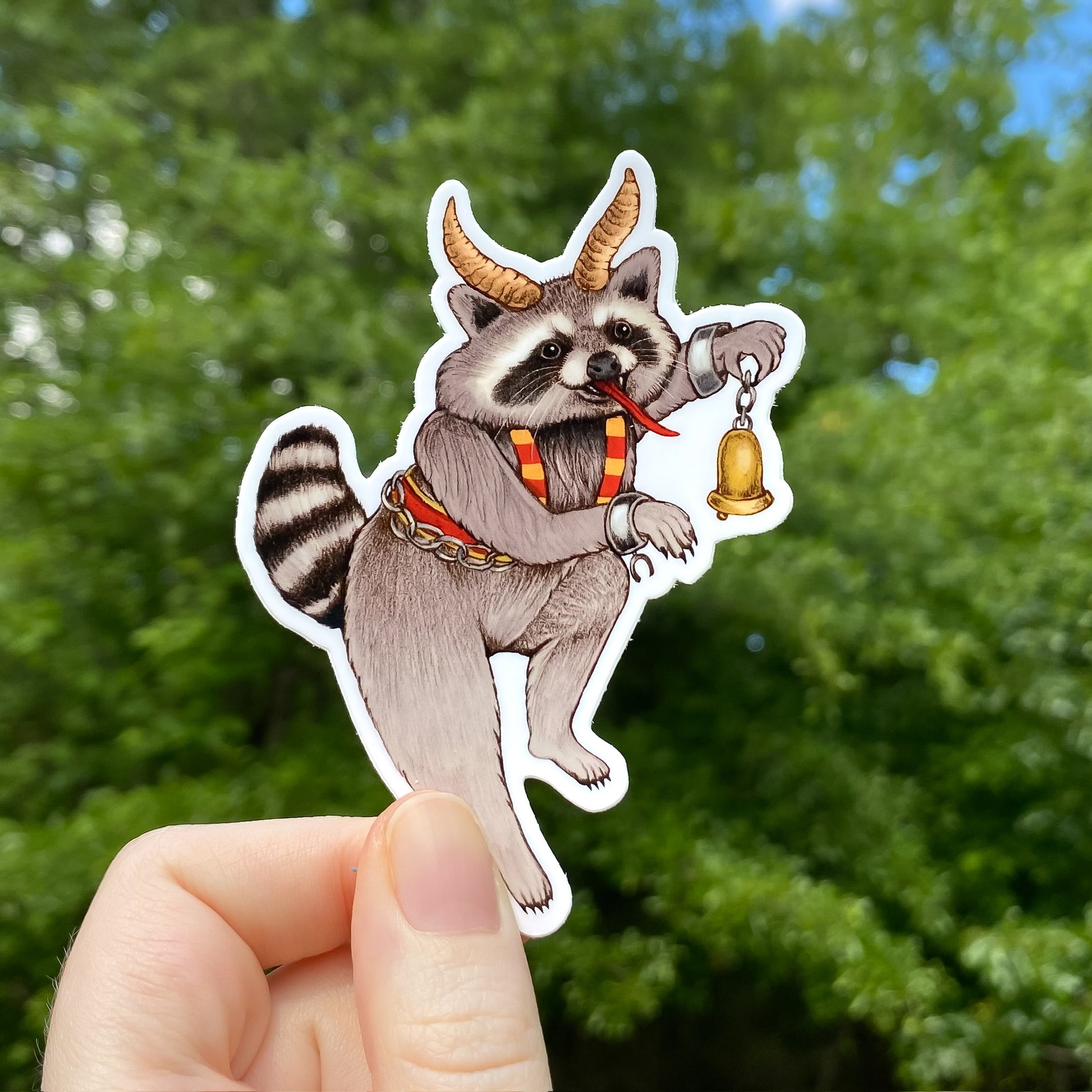 A hand holding a sticker of a raccoon dressed as Krampus