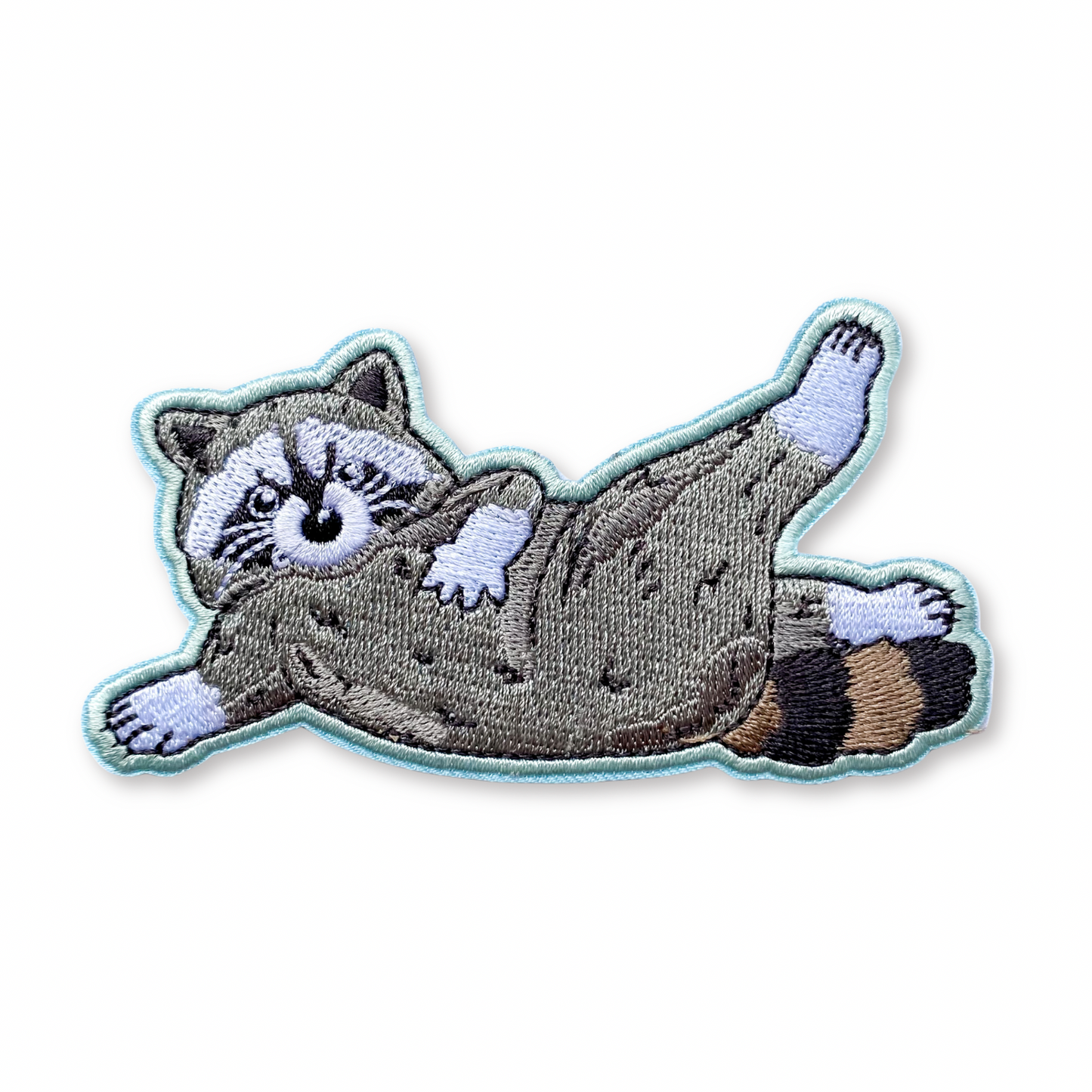 Embroidered patch of a lounging raccoon on a white background