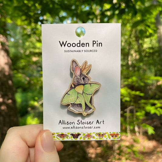 A wooden pin of an eastern cottontail with luna moth wings on packaging that reads Wooden Pin, Sustainably Sourced.
