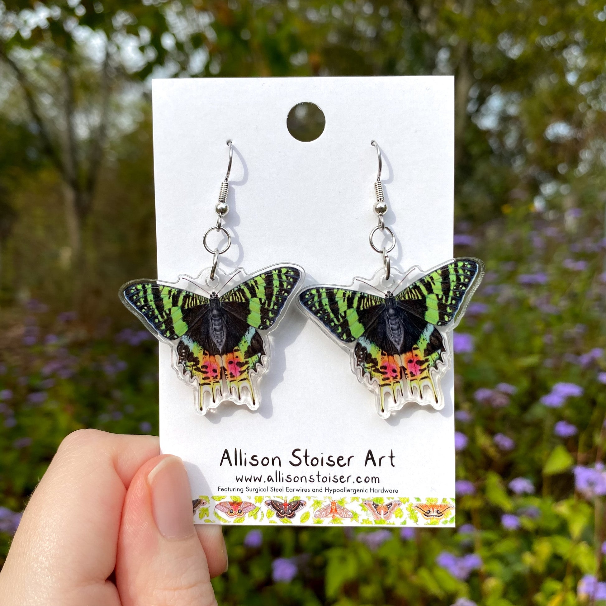 Madagascan sunset moth earrings on a card held by a hand with a natural background