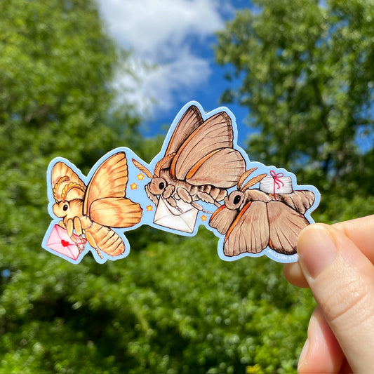 A hand holding a vinyl sticker with three mail moths 