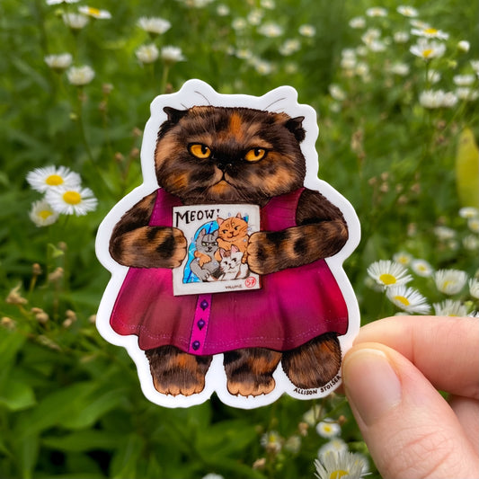 Sticker of a cat in a pink dress holding a manga book held in front of a green field with flowers