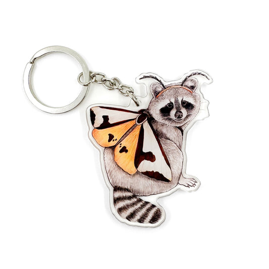 A keychain featuring an illustration of a raccoon dressed like a clymene moth