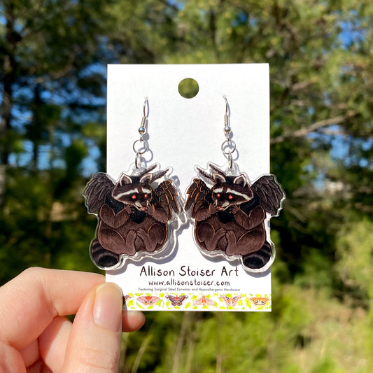 Earrings with acrylic charms of raccoons dressed up as mothman