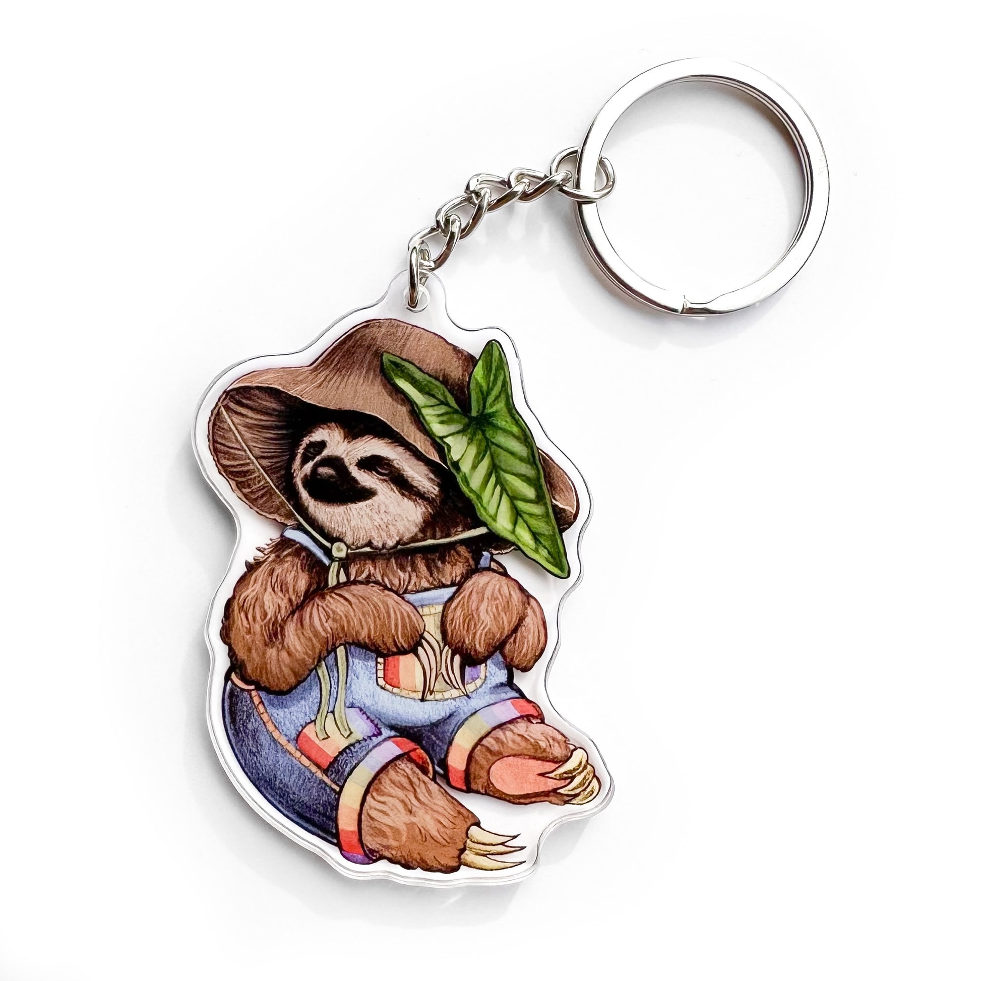 A keychain of a sitting sloth in overalls and with a mushroom hat on a white background.