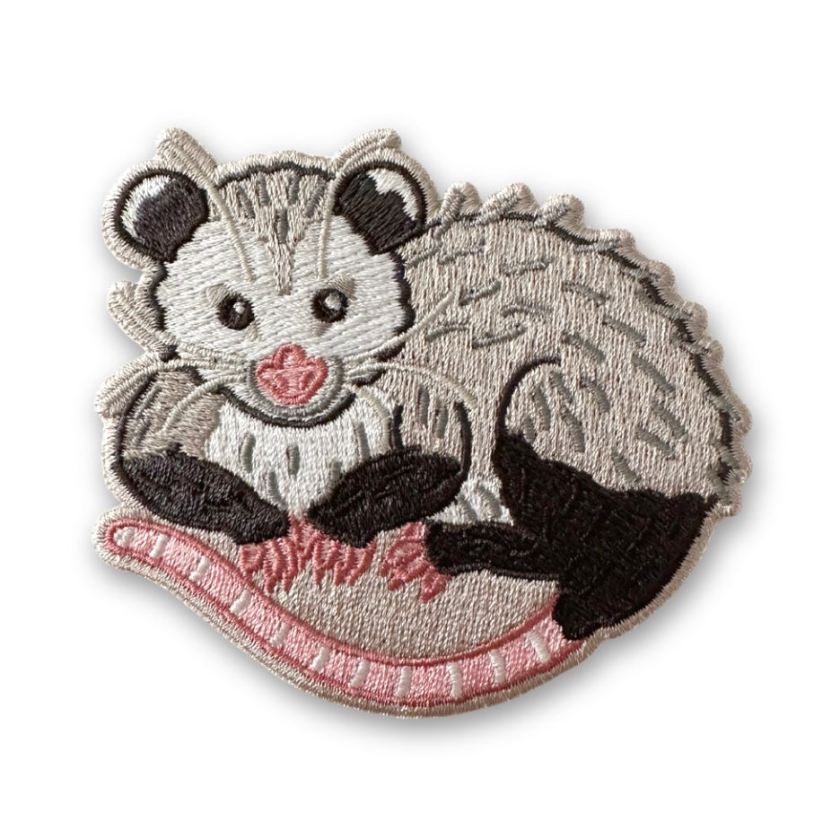 An embroidered patch of an opossum on a white background. 