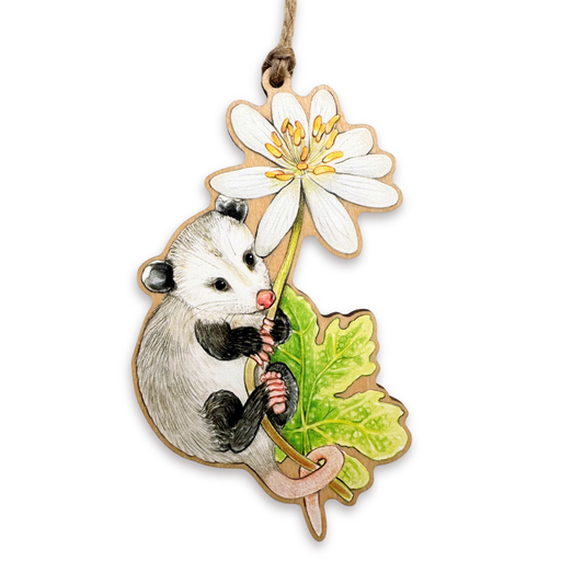A wooden ornament of an opossum on a bloodroot flower