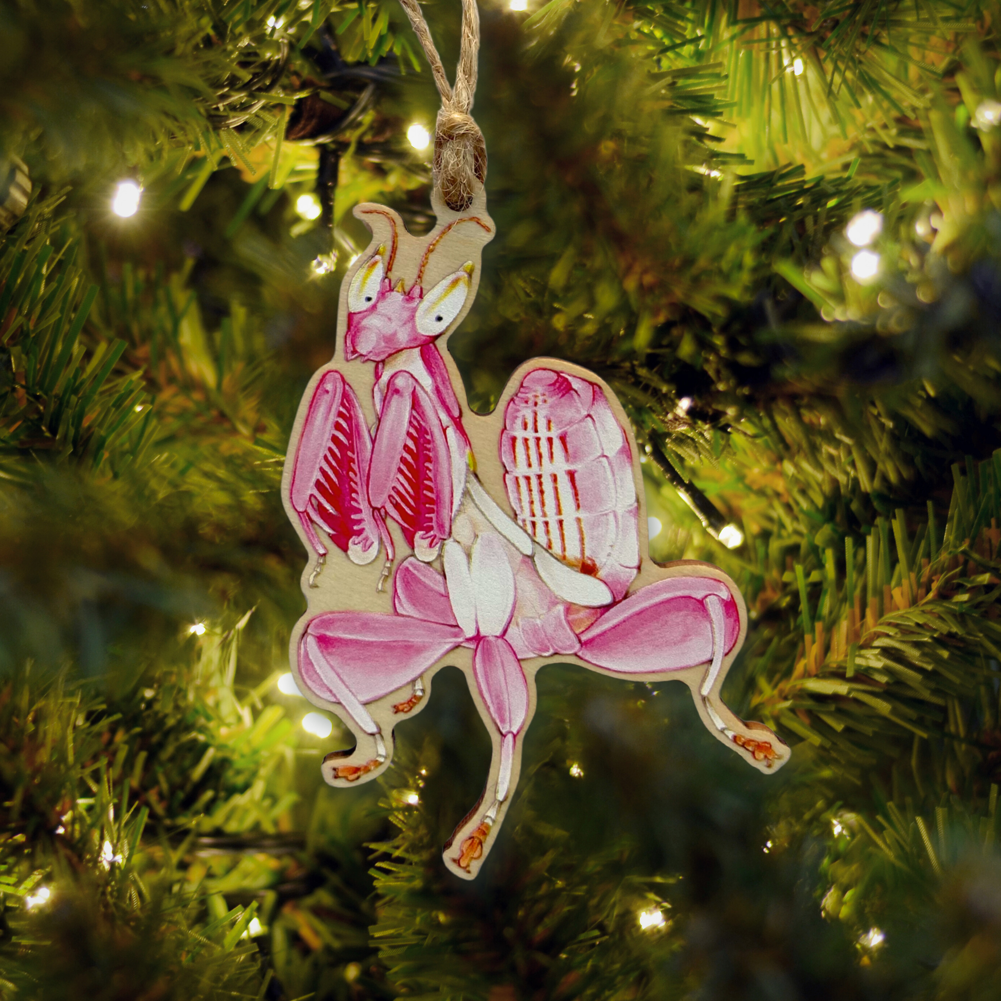 Decorative pink orchid mantis ornament hanging on a Christmas tree.