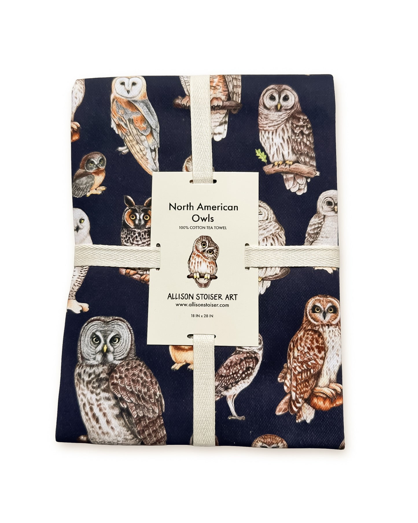 A tea towel featuring a detailed print of various North American Owls on a dark navy blue background. The fabric is wrapped with a white ribbon.