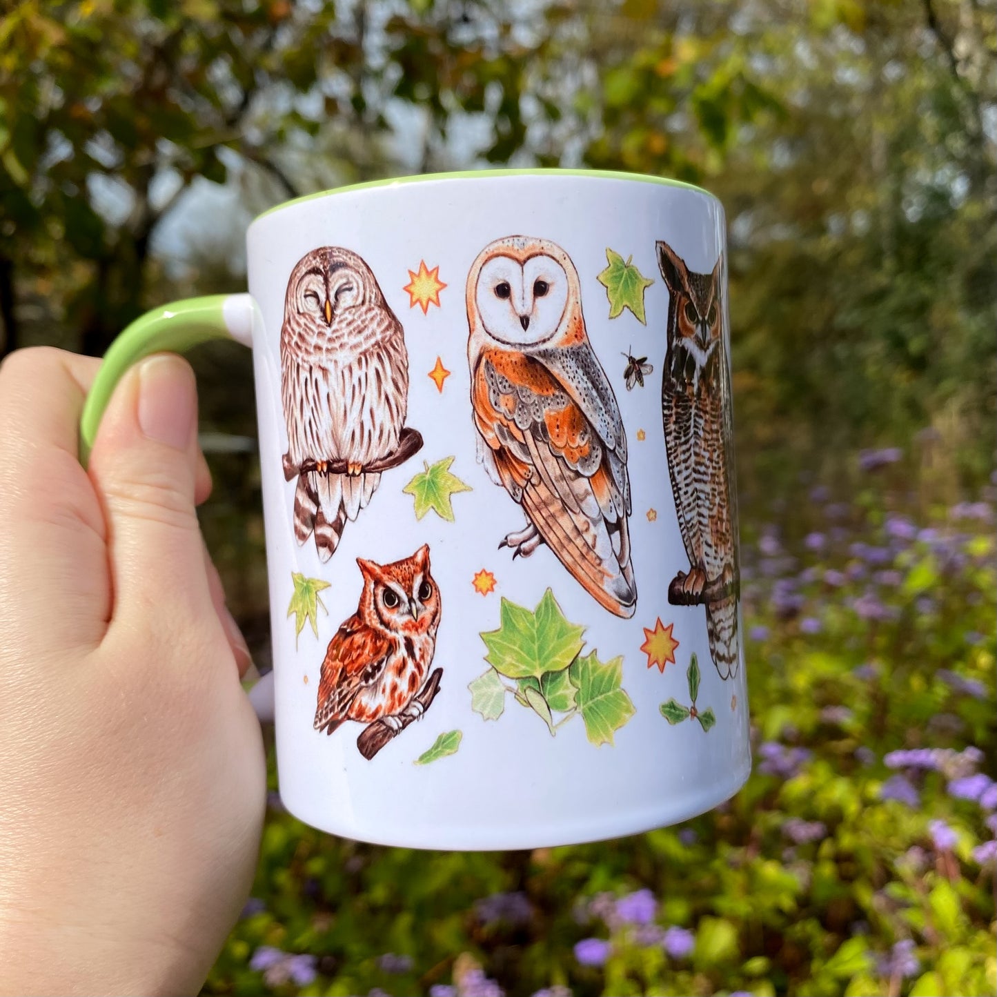 Mug with owl illustrations held in a hand against a natural background