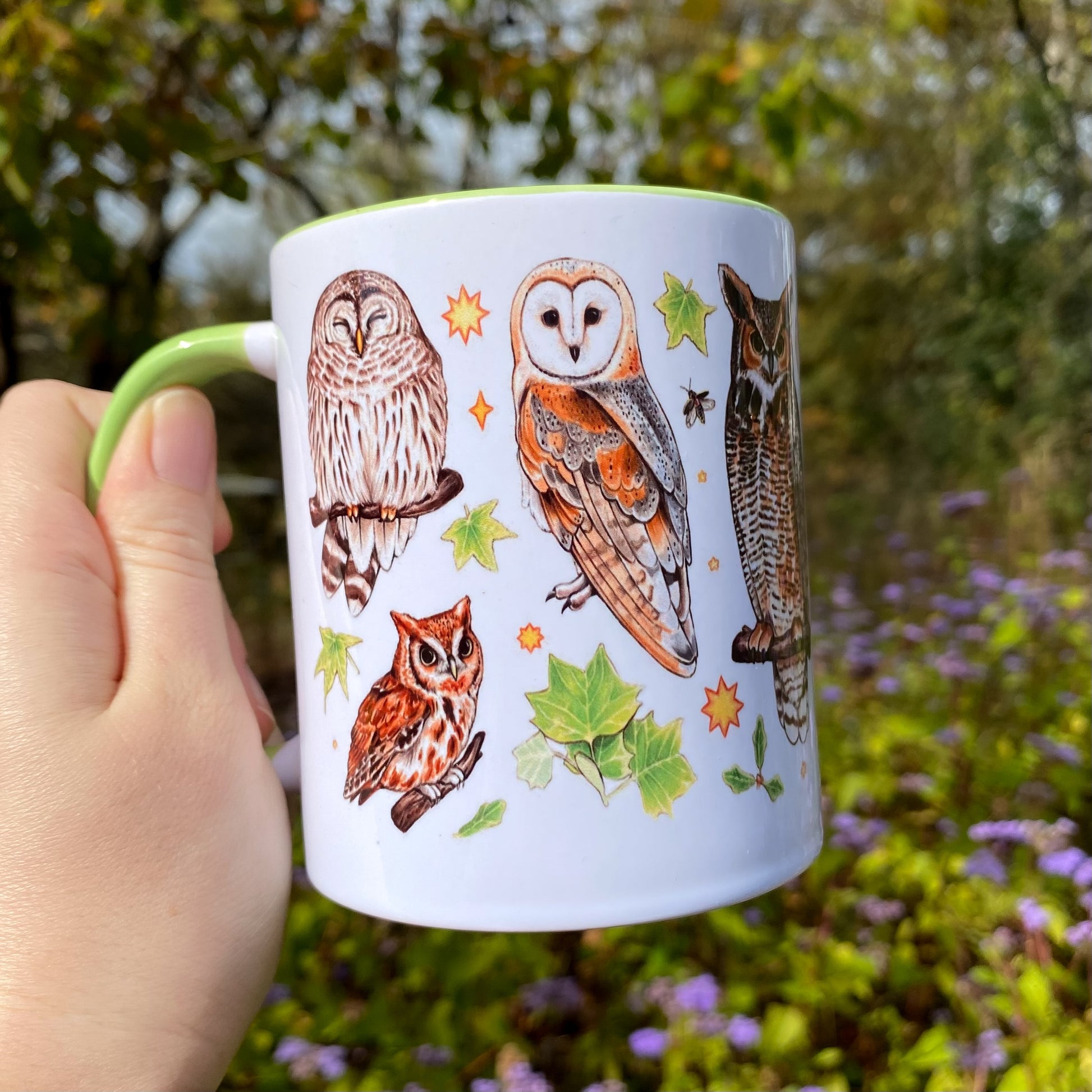 Mug with owl illustrations held in a hand against a natural background