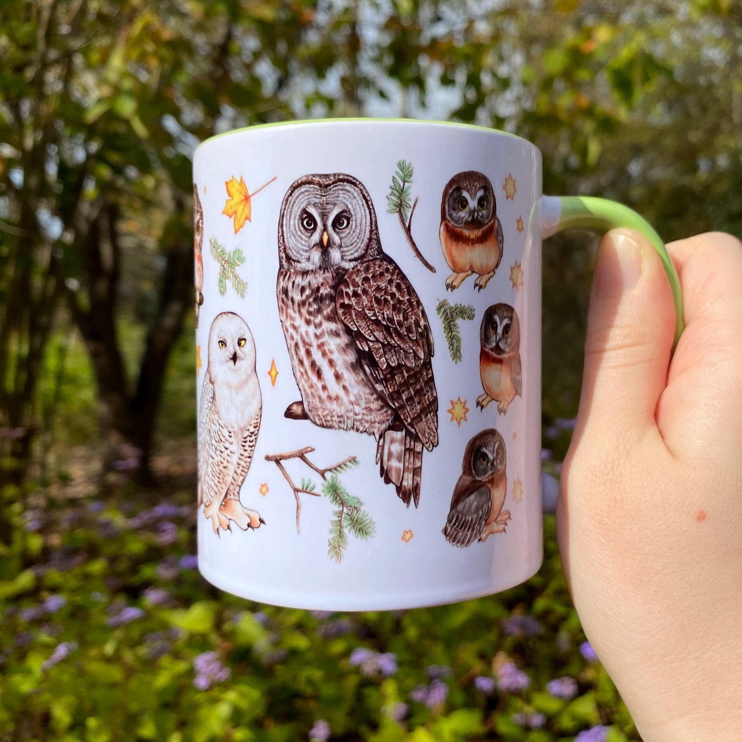 Mug with owl illustrations held by a hand in a natural setting
