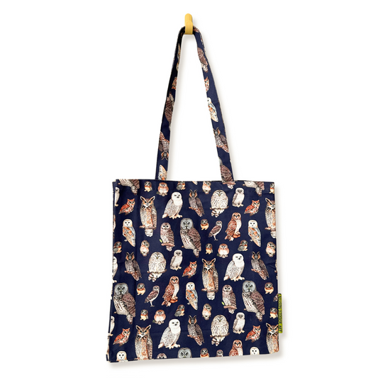 A dark blue fabric tote bag with an all-over print of various owl illustrations in brown, white, and gray, hanging from a small yellow hook on a white background.