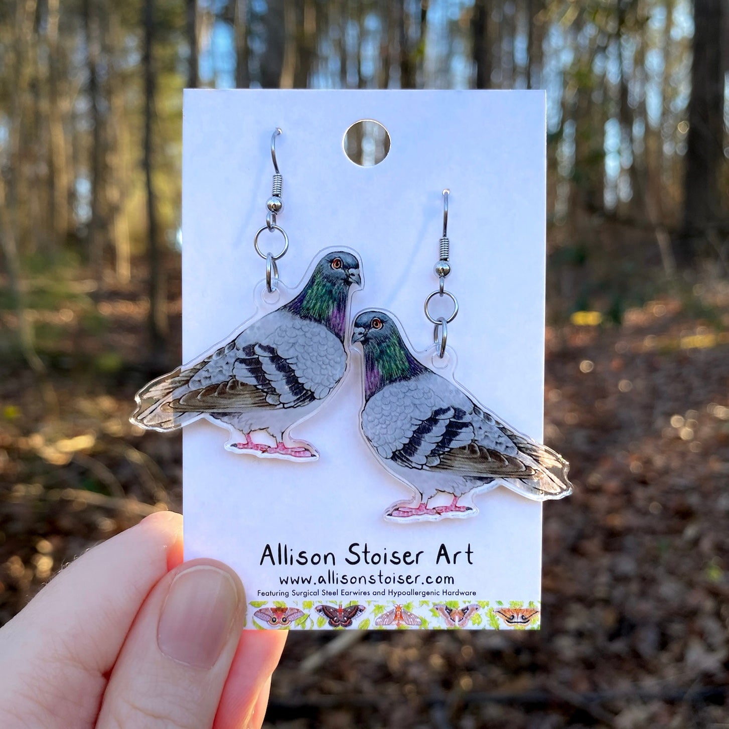 Pigeon earrings on a card held by a hand with a forest background