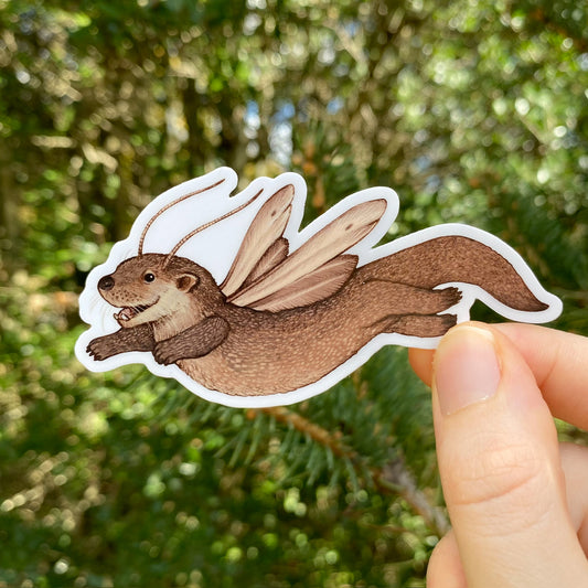 A hand holding a sticker of a flying otter with plume moth wings