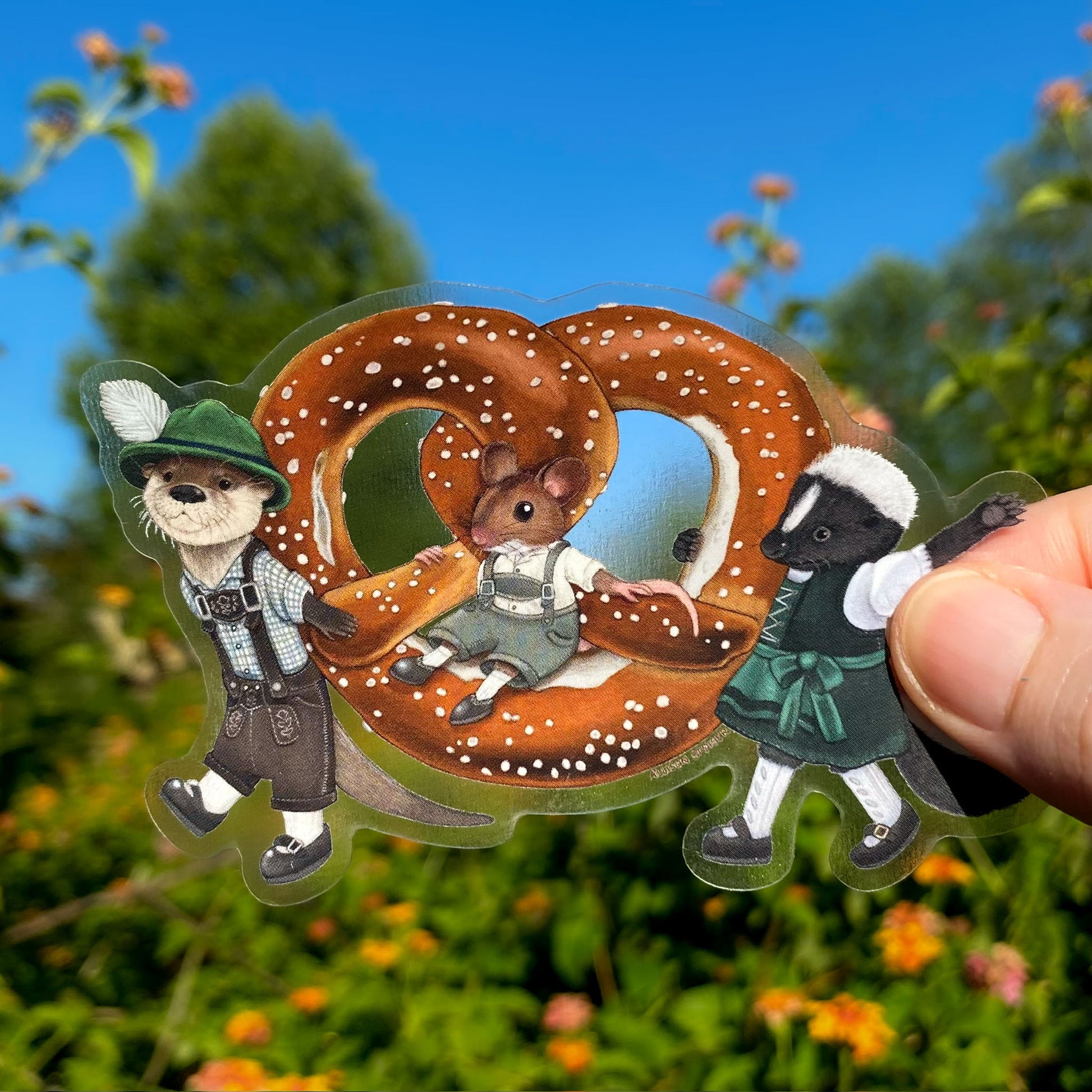 Sticker of an otter, mouse, and skunk parading a large pretzel against a natural background