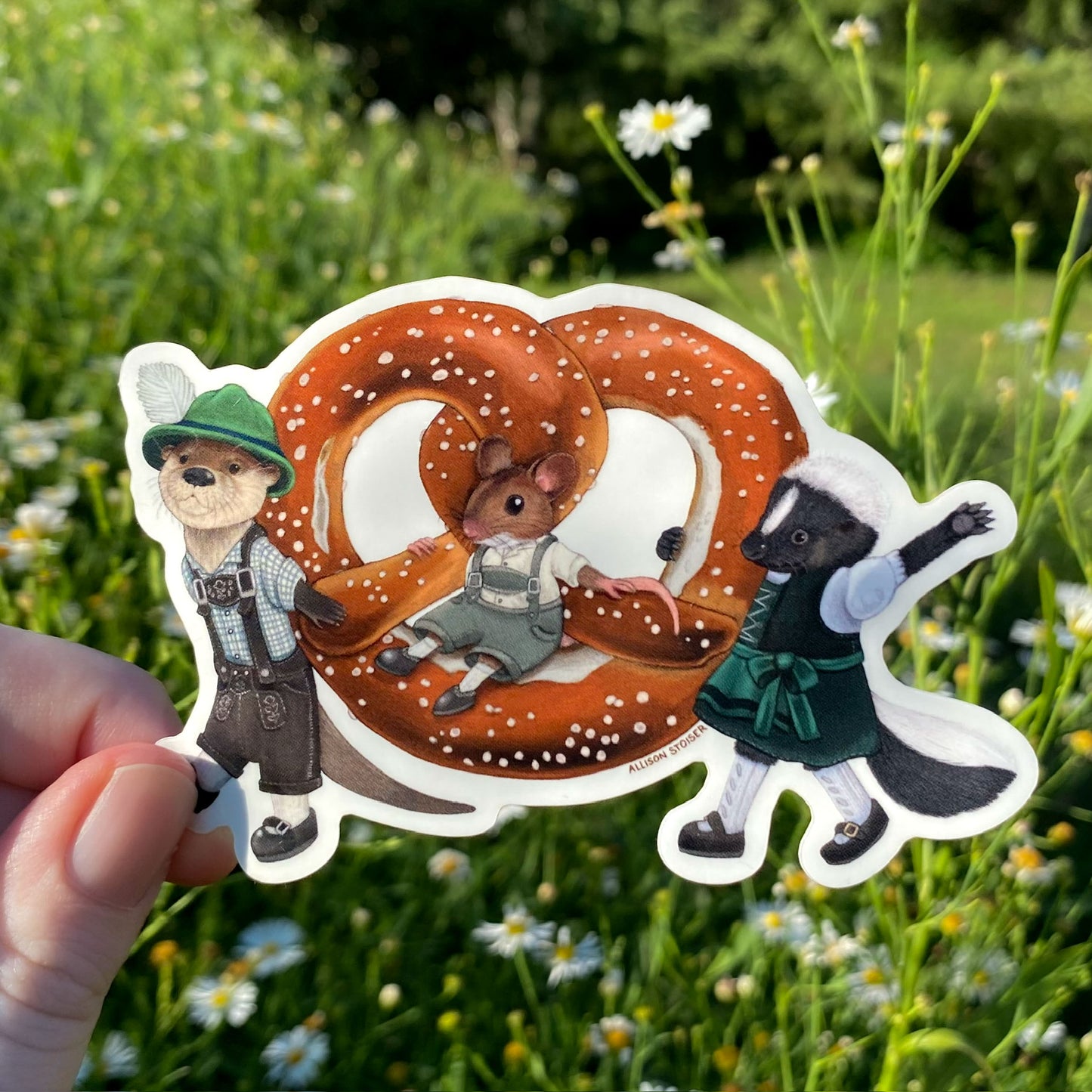 Sticker of an otter, mouse, and skunk parading a large pretzel against a natural background