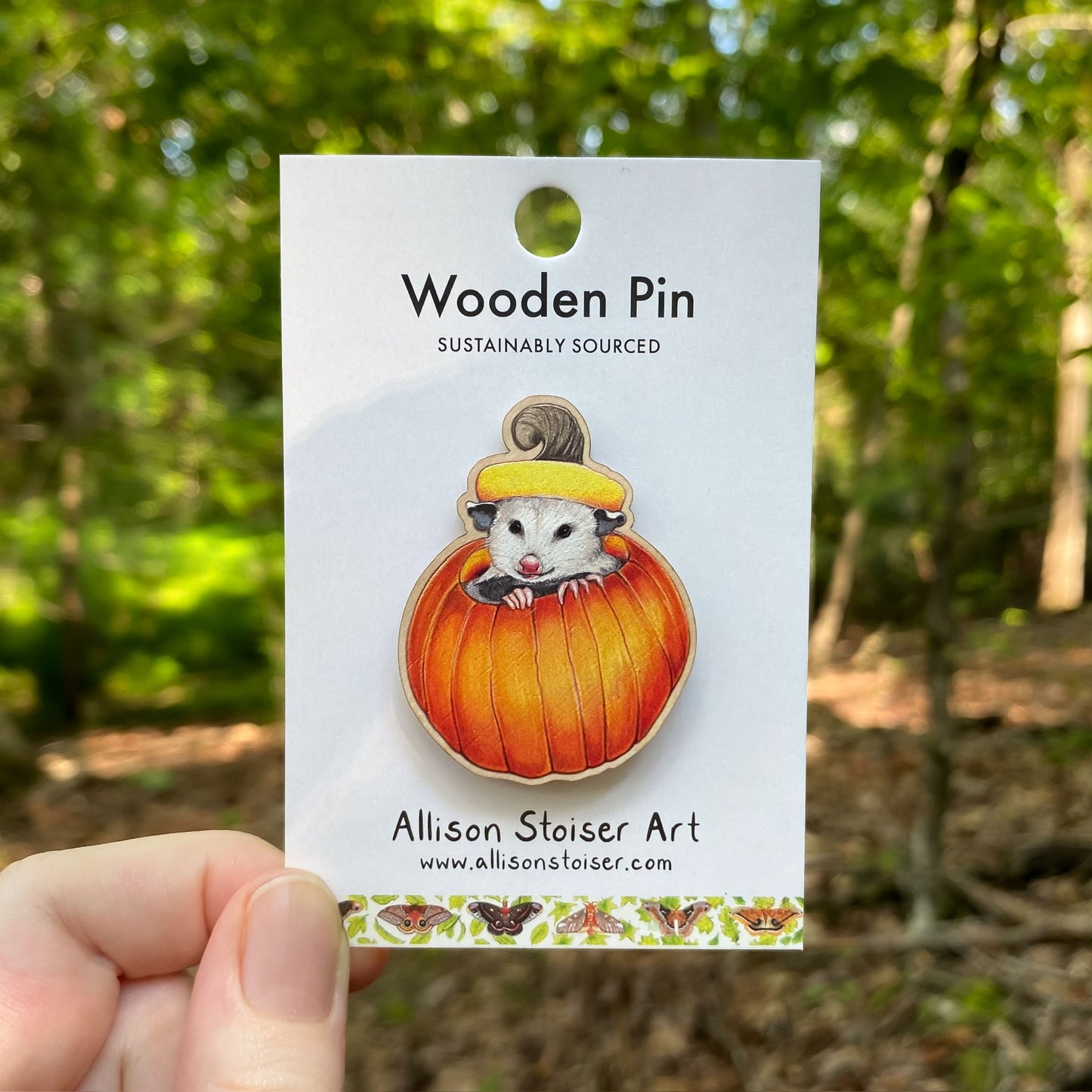 Wooden pin of an opossum in a pumpkin on a card with a forest background
