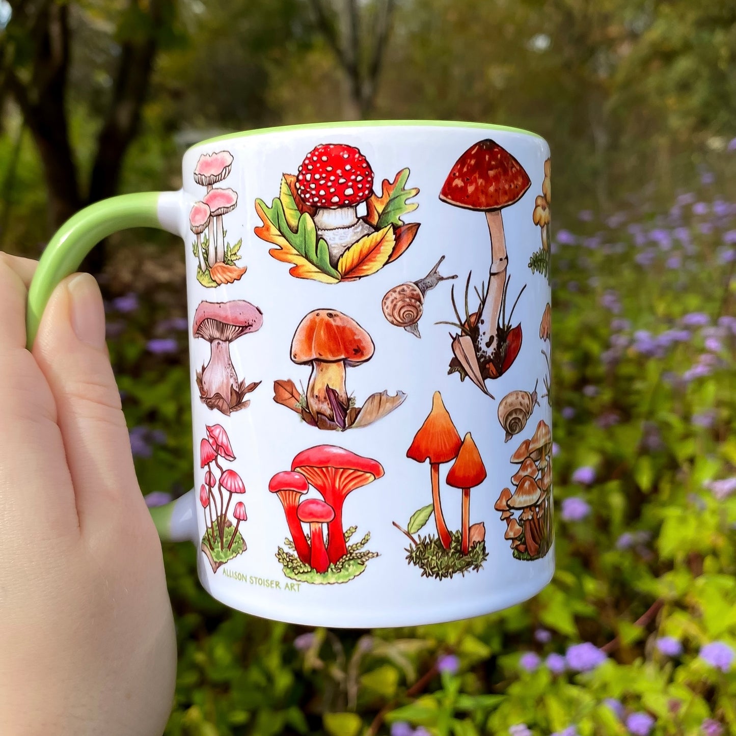Mug with mushroom illustrations held in front of a natural background