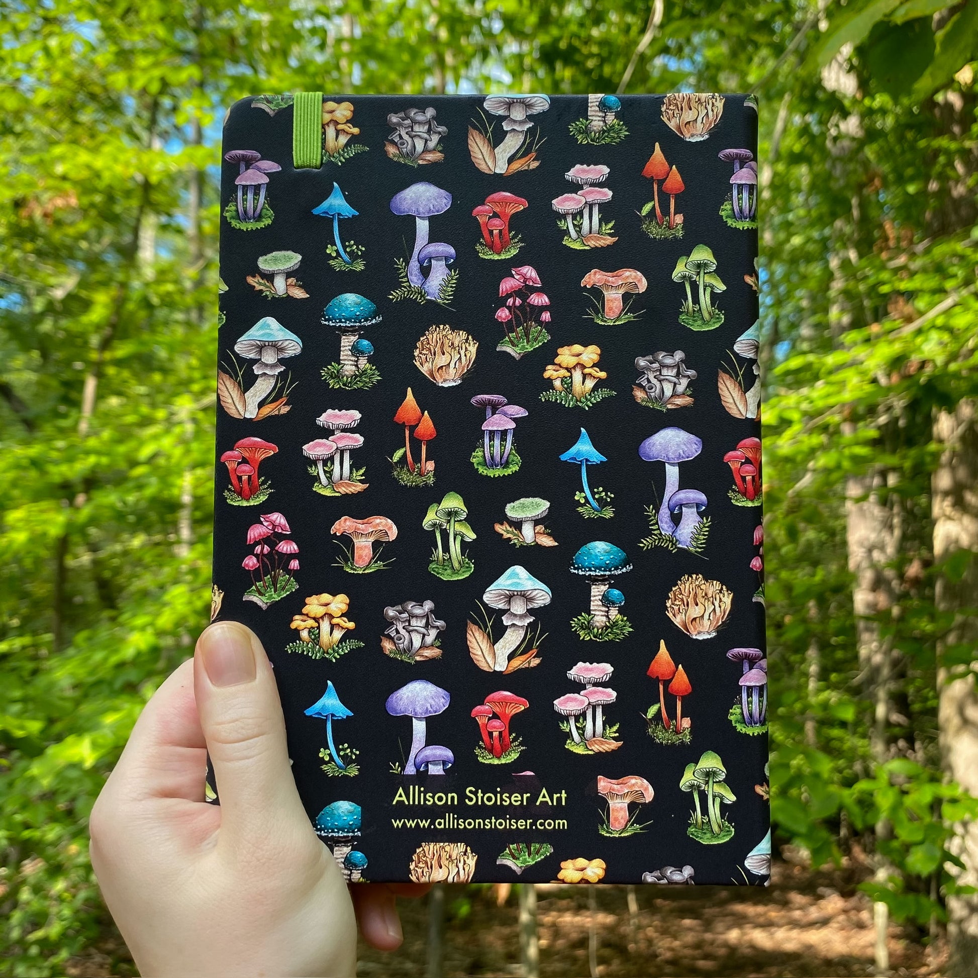 Notebook with colorful mushroom pattern held in front of a forest background