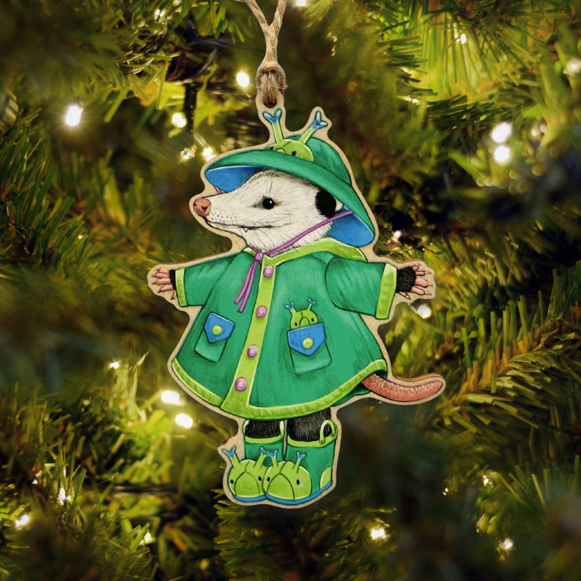 Decorative Christmas ornament of an opossum in a green raincoat hanging on a tree.