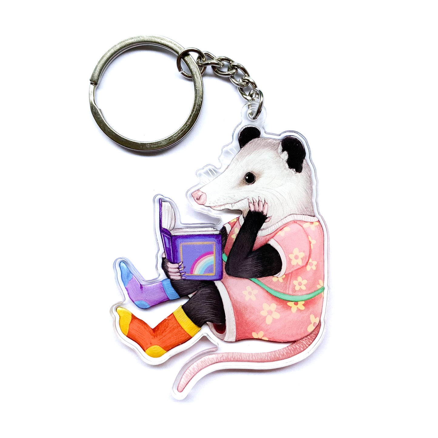 Keychain with an opossum reading a book on a white background