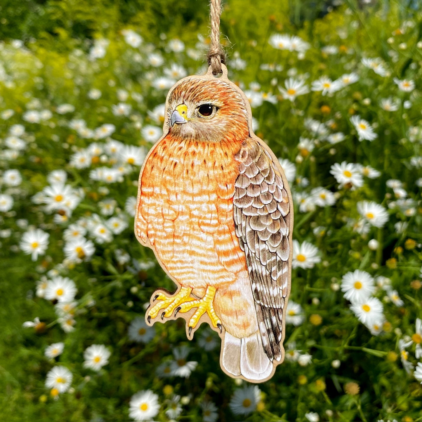 Decorative red-shouldered hawk ornament hanging against a background of greenery and white flowers