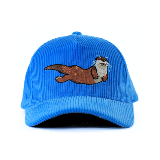 The front of a blue corduroy baseball cap with an embroidered river otter on a white background.