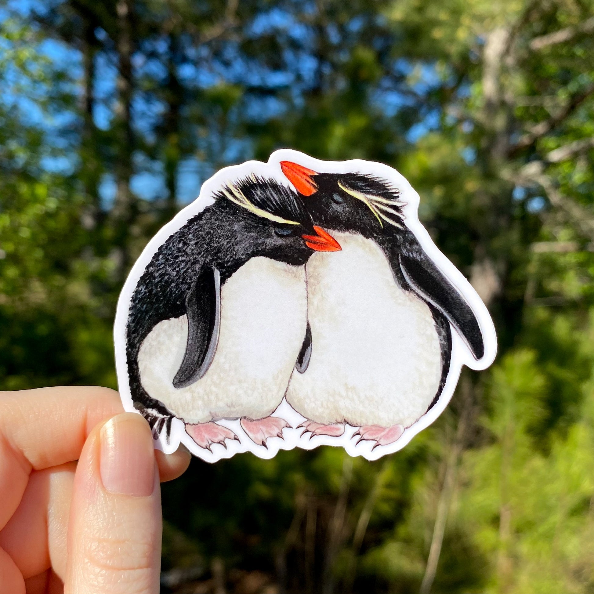A vinyl sticker with two rockhopper penguins displayed against a natural background.