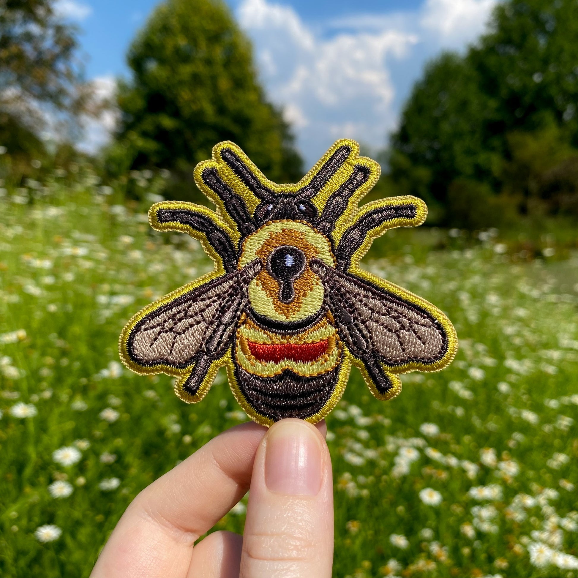 A hand holding an embroidered patch of a rusty-patched bumble bee.