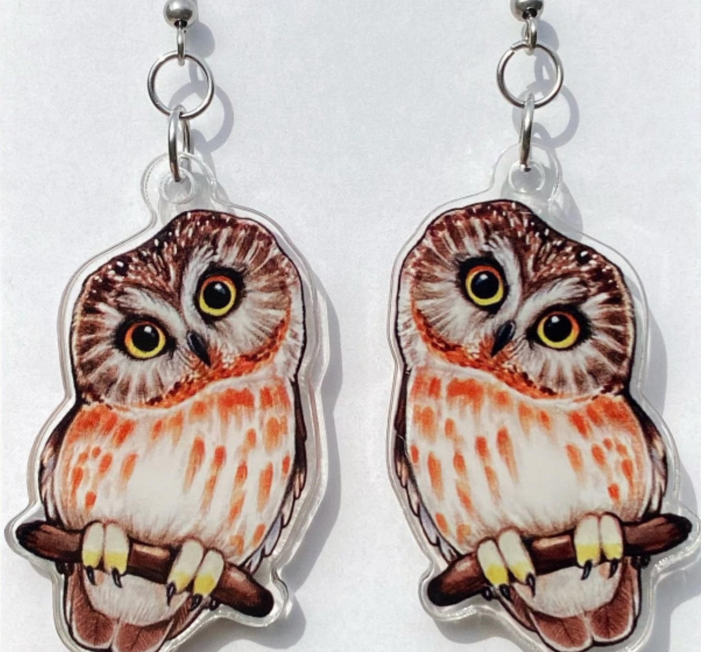 A close-up of a pair of acrylic saw-whet owl earrings.