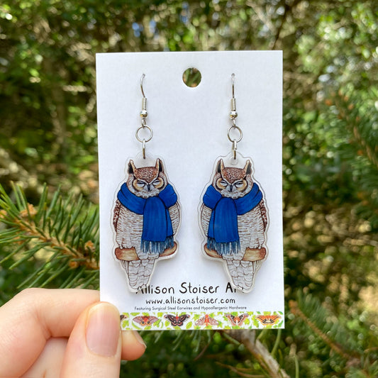 A hand holding a pair of scarf great horned owl acrylic earrings