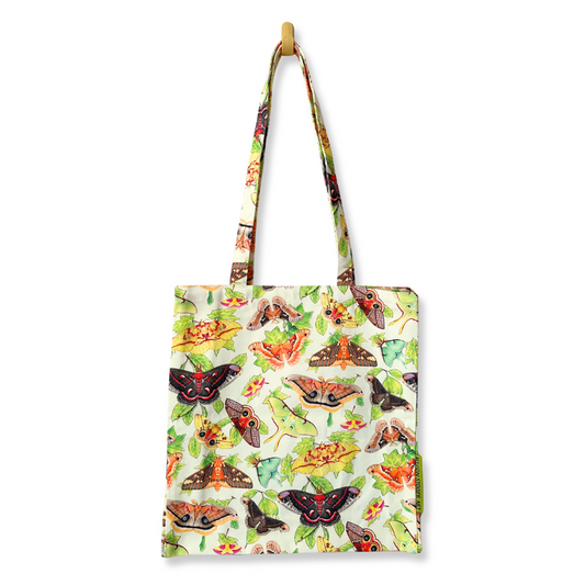 A canvas tote bag with a white background covered in a pattern of moths and leaves, hanging from a wooden peg on a black background.