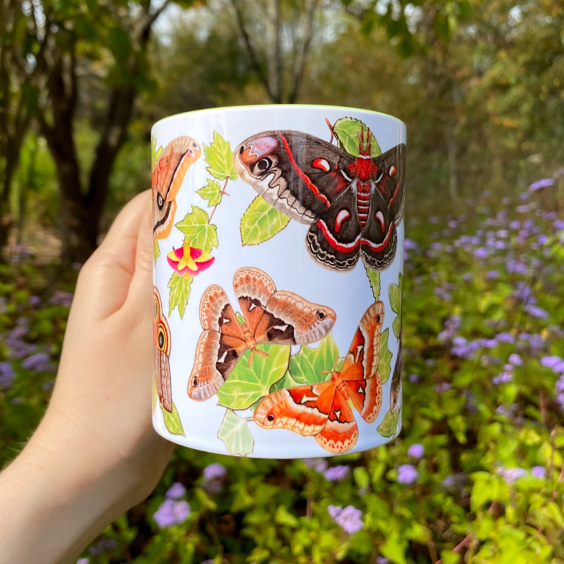 Mug with silkmoths held in front of a natural background with flowers and trees